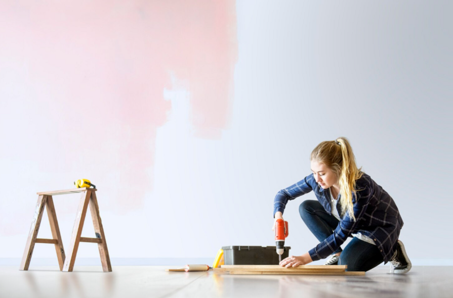 Junge Frau arbeitet mit einer Bohrmaschine an einem Holzstück in einem frisch renovierten Raum.